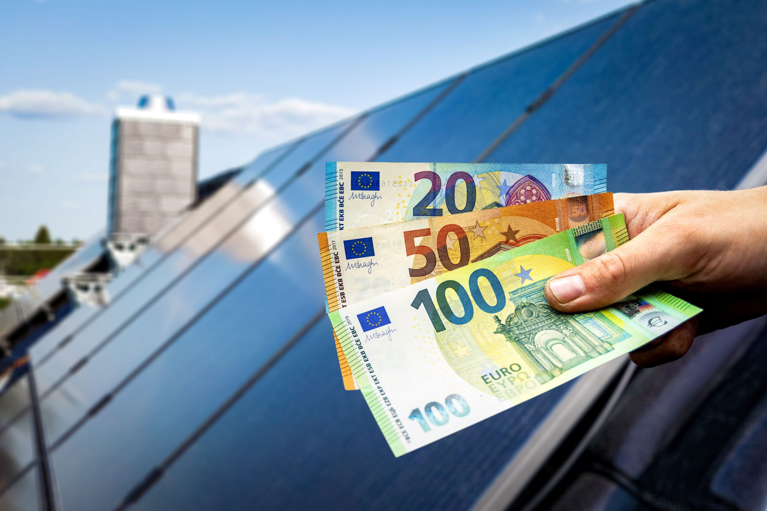 Eine Person hält Geld in ihrer Hand und im Hintergrund ist eine Solaranlage 