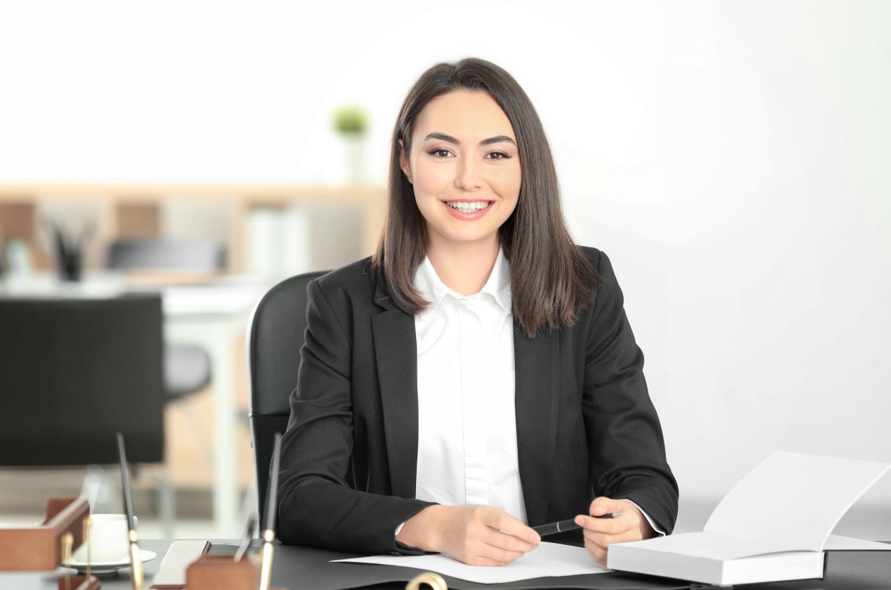 Eine lächelnde Anwältin der Kanzlei Ra-Hartung sitzt in einem modernen Büro mit Dokumenten und zeigt Kompetenz und Freundlichkeit.