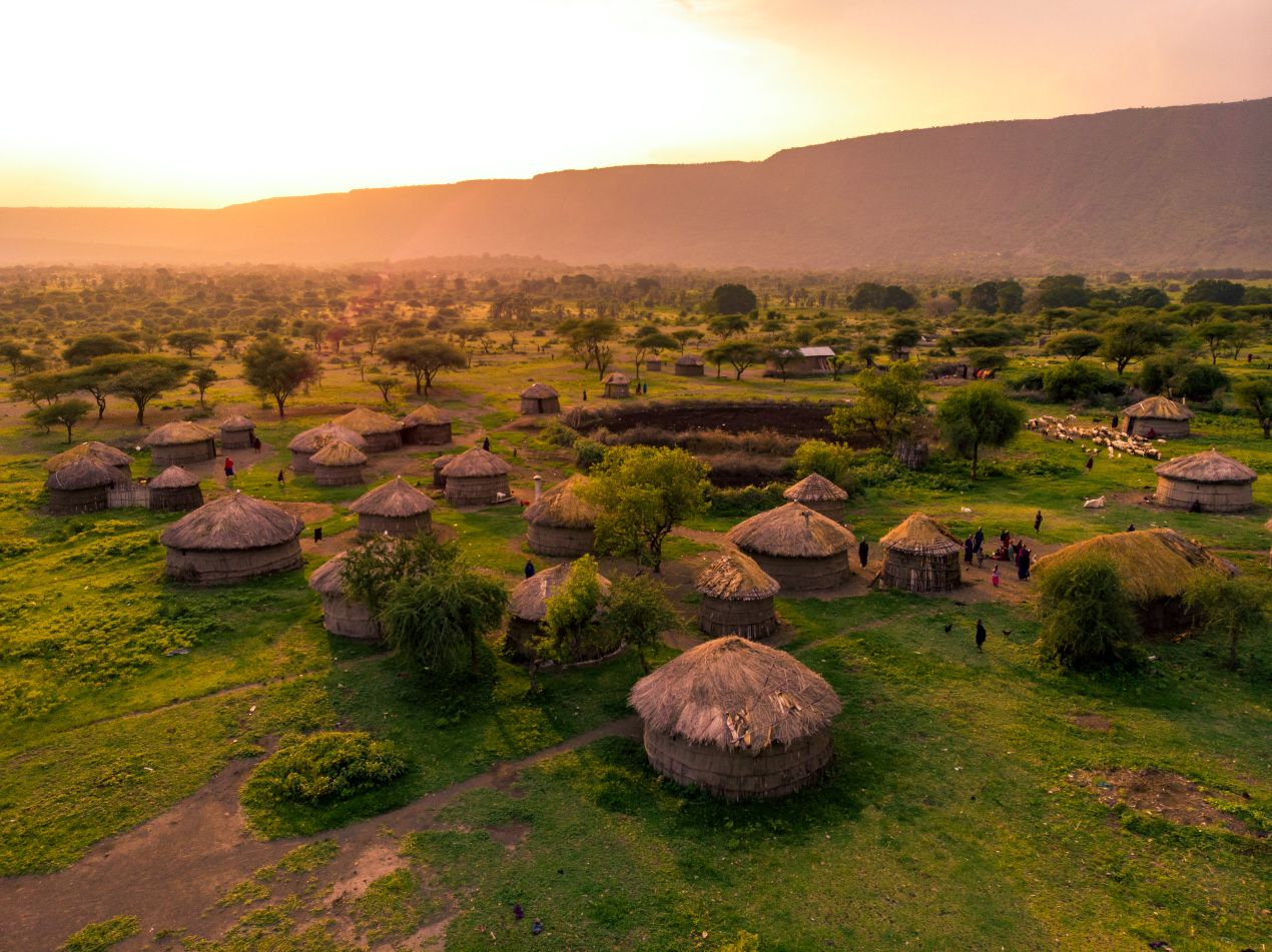 Eine Luftaufnahme eines traditionellen Dorfes mit Rundhütten in der Landschaft Tansanias, perfekt für kulturelle Erlebnisse während einer Tansania Safari.