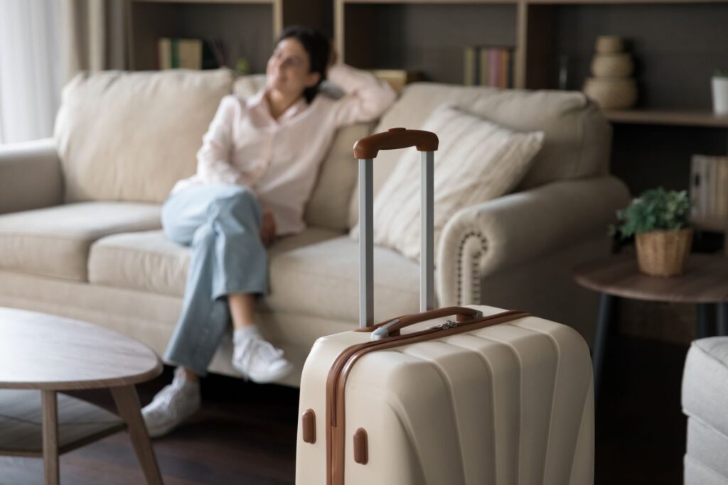 Gemütliche Ferienwohnung – eine entspannte Frau sitzt auf dem Sofa, während ihr Koffer im Vordergrund steht.